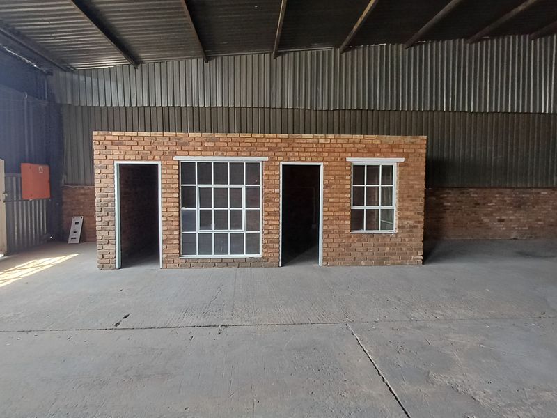 Spacious industrial warehouse interior featuring a central brick office structure, concrete flooring, and exposed steel roof trusses.