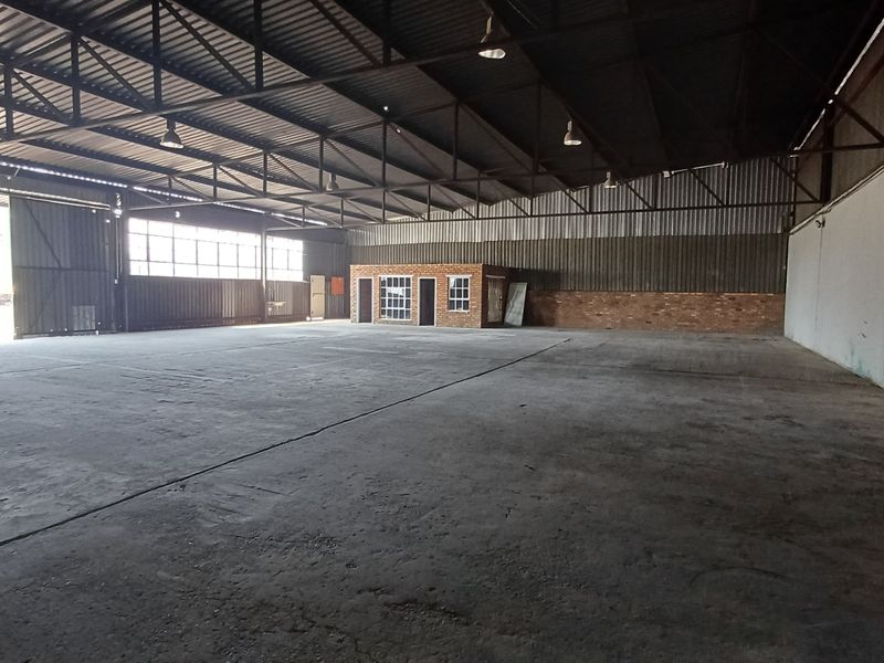 Spacious industrial warehouse featuring high ceilings, concrete flooring, and an integrated brick office enclosure, suitable for various commercial or storage applications.