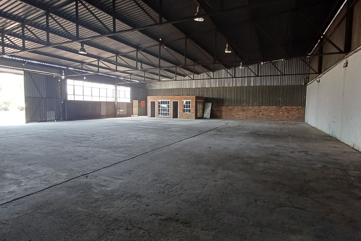 Spacious industrial warehouse featuring high ceilings, concrete flooring, and an integrated brick office enclosure, suitable for various commercial or storage applications.