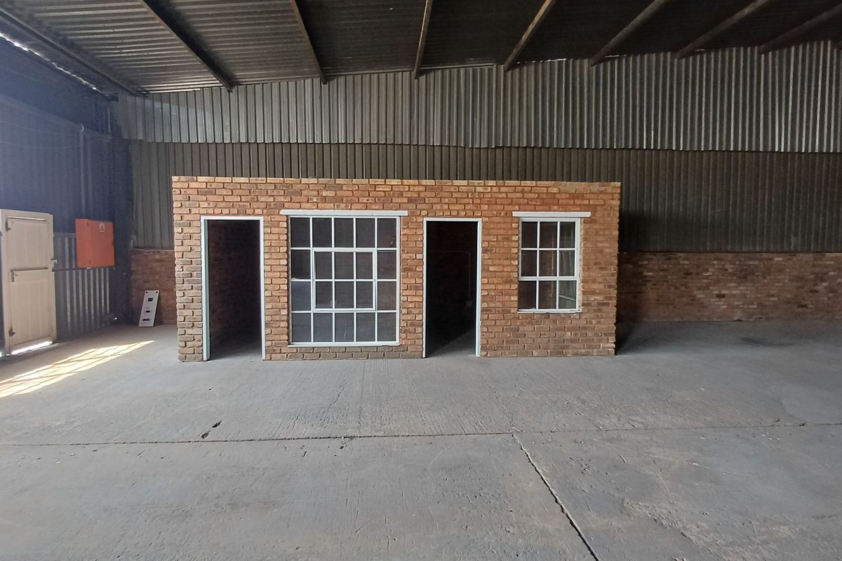 Spacious industrial warehouse interior featuring a central brick office structure, concrete flooring, and exposed steel roof trusses.