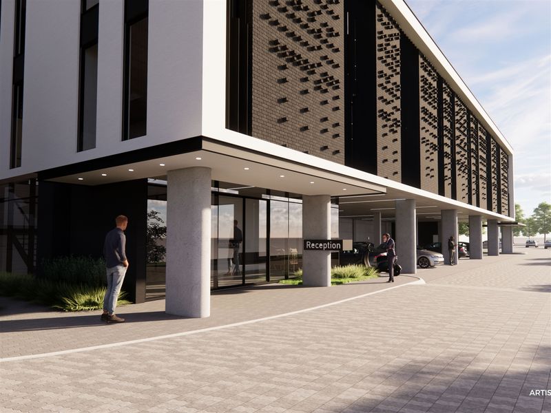 Modern industrial building exterior featuring a covered entrance, concrete support columns, glass facade, and paved driveway area.