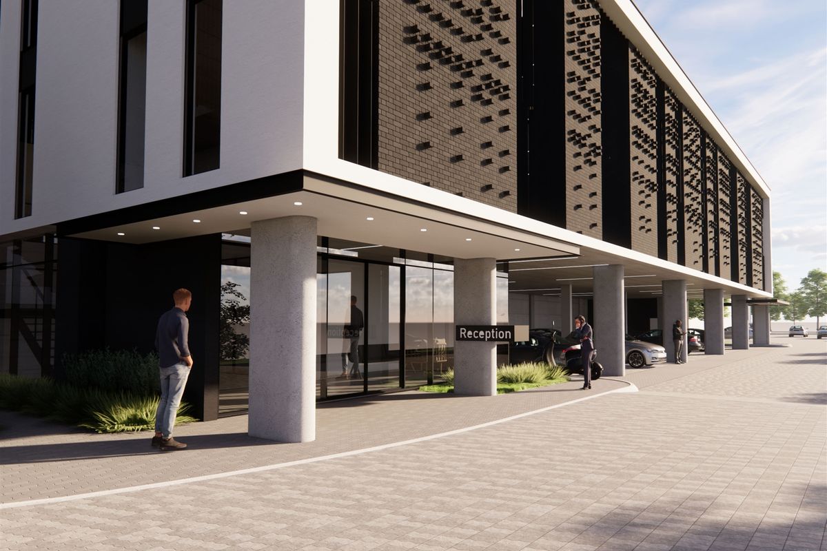 Modern industrial building exterior featuring a covered entrance, concrete support columns, glass facade, and paved driveway area.