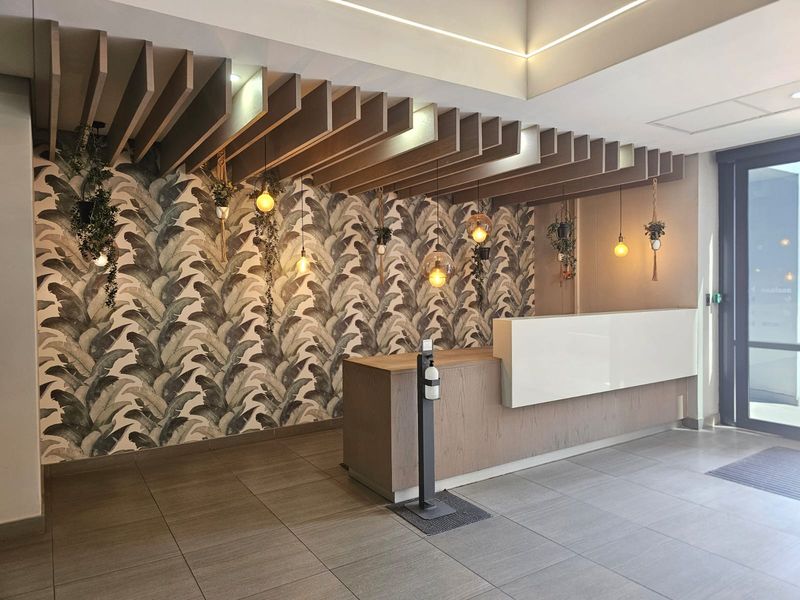 Modern office reception area featuring a sleek built-in desk, decorative ceiling slats, patterned feature wall, and professional tiled flooring.