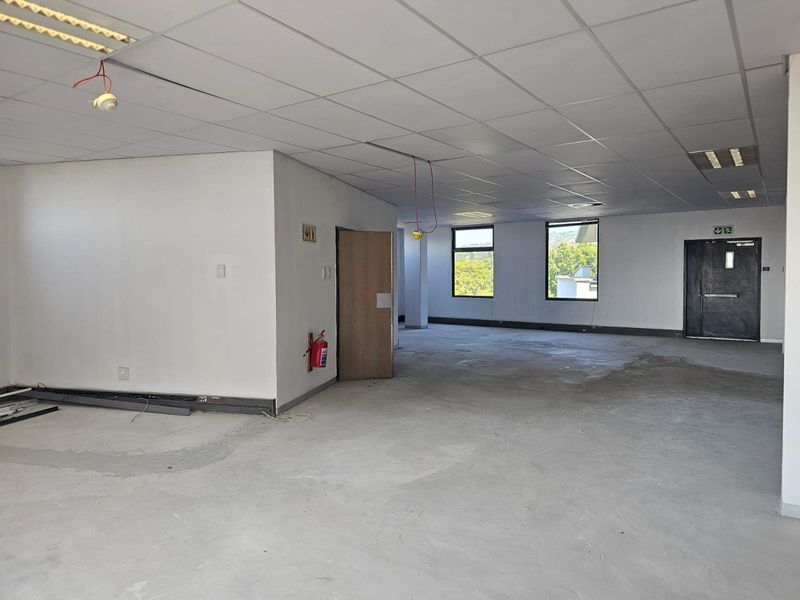 An open-plan office space featuring a suspended ceiling, emergency exit, and unfinished concrete flooring, ready for custom fit-out and flooring installation.