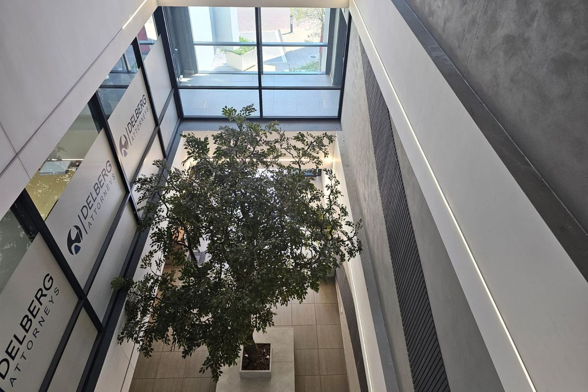 Modern office atrium featuring a double-volume space with large glass windows, sleek slatted wall detailing, and recessed linear lighting.
