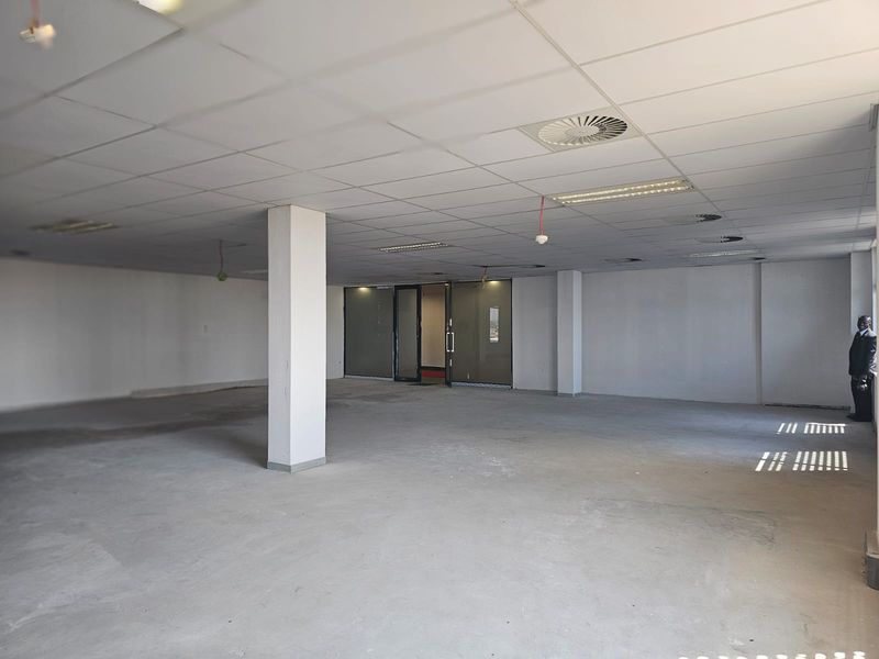 A spacious, open-plan office area featuring a suspended ceiling, recessed lighting, and structural columns, currently in a shell condition ready for fit-out.