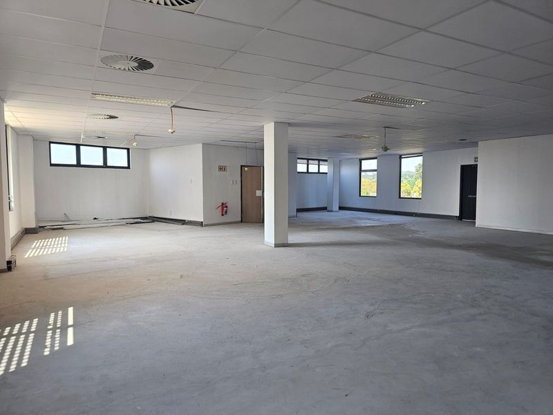 A large, open-plan office space featuring a suspended ceiling, recessed lighting, and structural columns, currently in a shell condition awaiting flooring and final finishes.