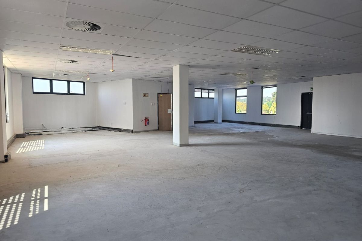 A large, open-plan office space featuring a suspended ceiling, recessed lighting, and structural columns, currently in a shell condition awaiting flooring and final finishes.