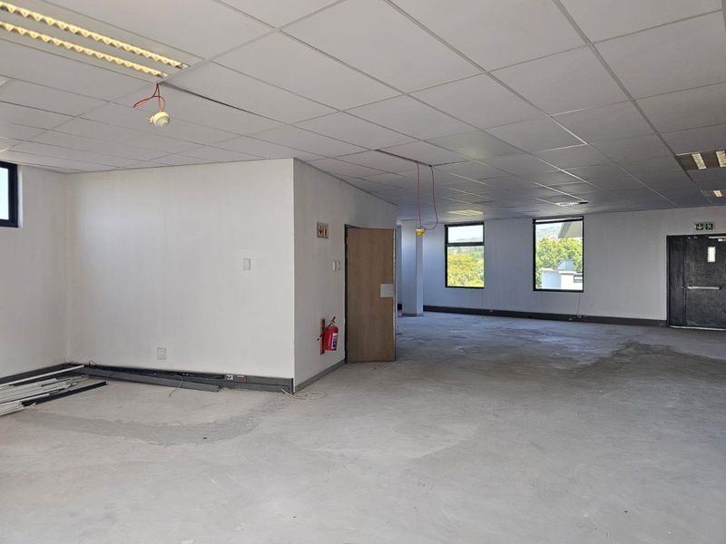 A spacious, open-plan office area featuring a suspended ceiling, recessed lighting, and large windows, currently in a shell condition awaiting final flooring finishes.