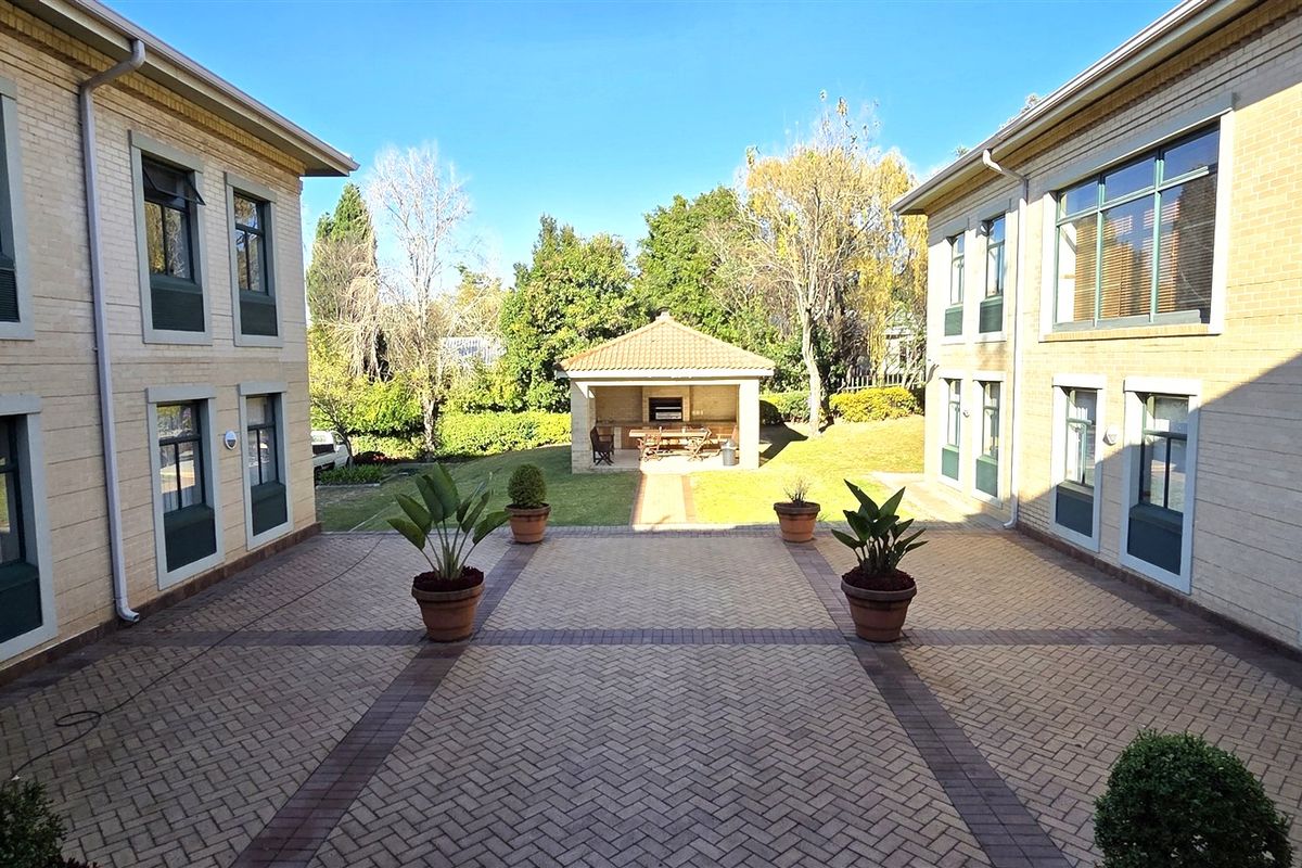 A view of the office complex courtyard featuring paved walkways, landscaped garden areas, and a covered outdoor entertainment structure.