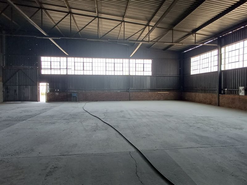 Spacious industrial warehouse unit featuring high ceilings with exposed steel trusses, concrete flooring, and large windows providing ample natural light.