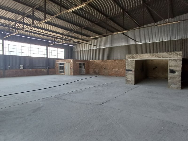 Spacious industrial warehouse unit featuring high ceilings with exposed steel trusses, concrete flooring, and large steel-framed windows providing ample natural light.