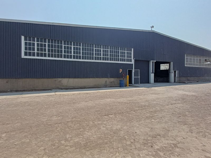 Industrial warehouse exterior featuring corrugated metal cladding, large steel-framed windows, and a spacious concrete apron for vehicle access.