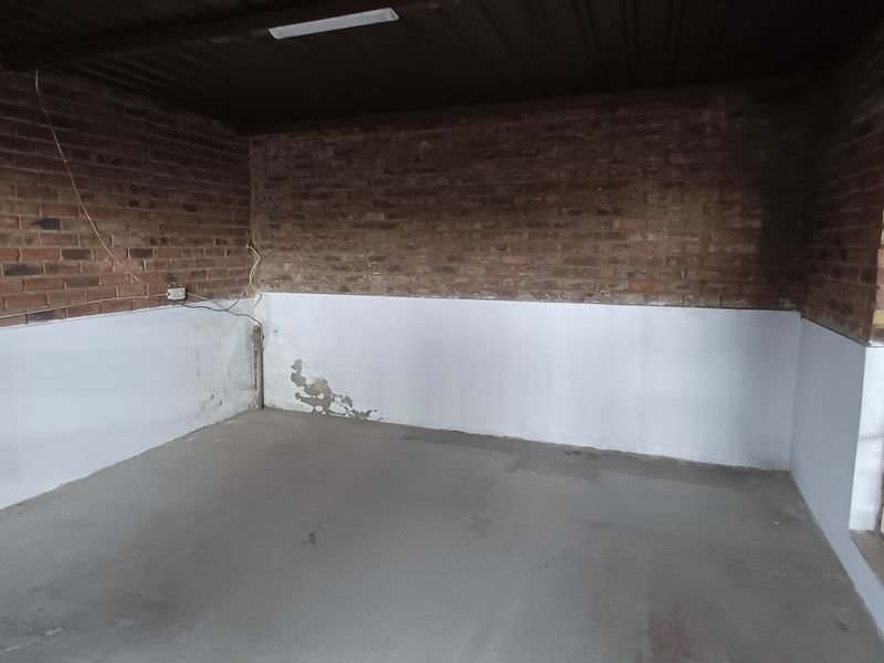 An empty industrial utility space featuring exposed brick walls, concrete flooring, and large steel-framed windows, suitable for storage or workshop use.