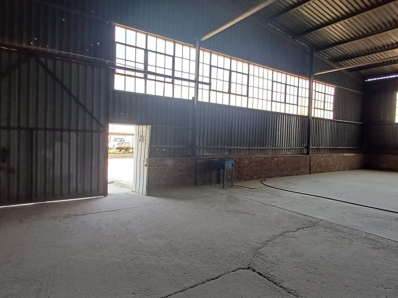 Spacious industrial utility area featuring corrugated metal walls, exposed steel roof trusses, large industrial windows, and concrete flooring.