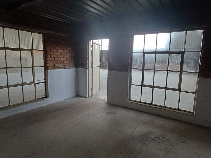 An empty industrial utility space featuring exposed brick walls, large steel-framed windows, and a corrugated metal ceiling with concrete flooring.