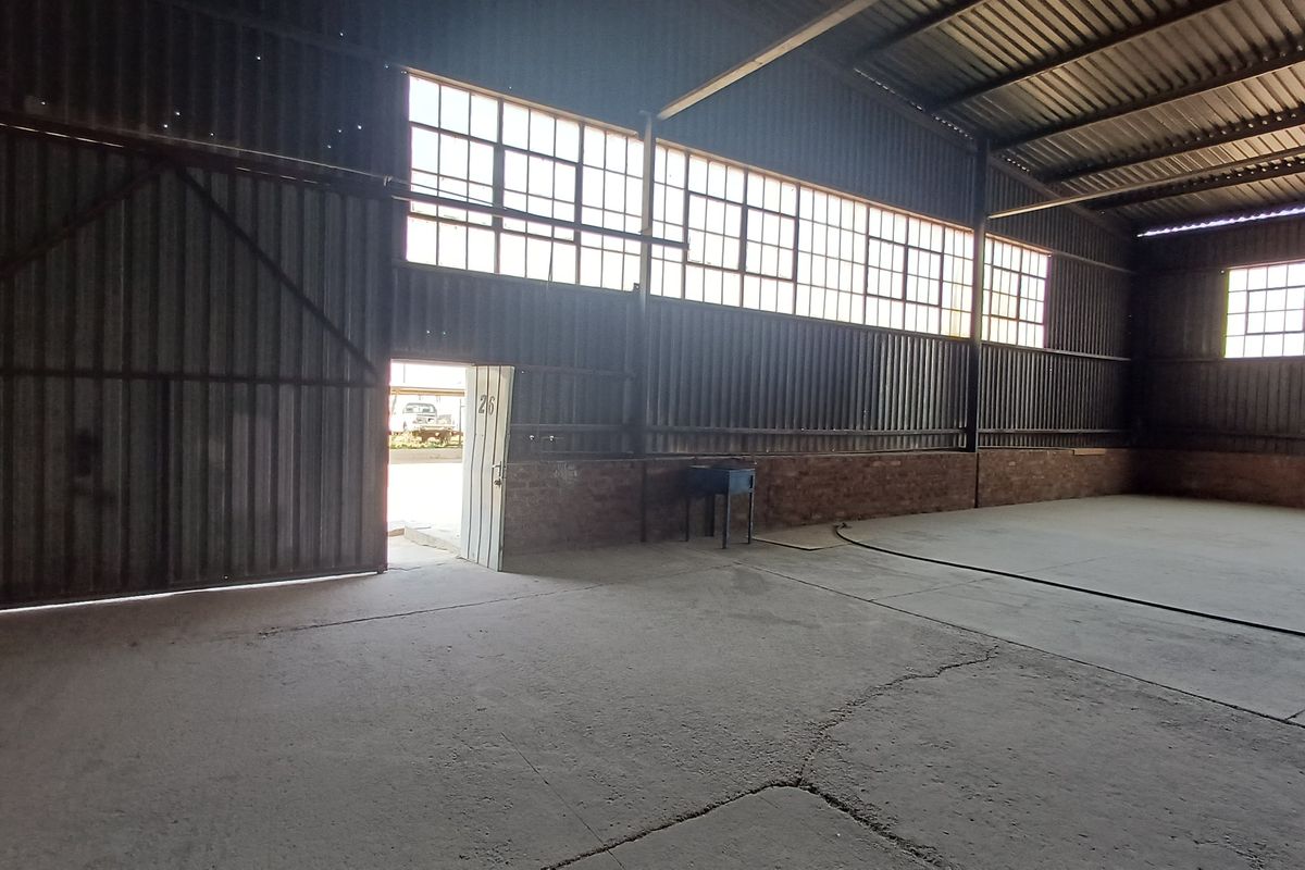 Spacious industrial utility area featuring corrugated metal walls, exposed steel roof trusses, large industrial windows, and concrete flooring.