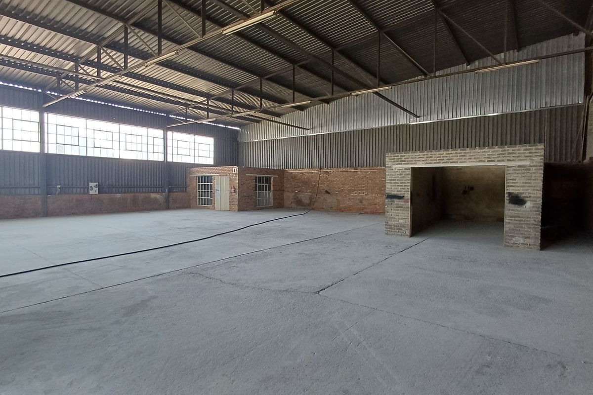 Spacious industrial warehouse unit featuring high ceilings with exposed steel trusses, concrete flooring, and large steel-framed windows providing ample natural light.