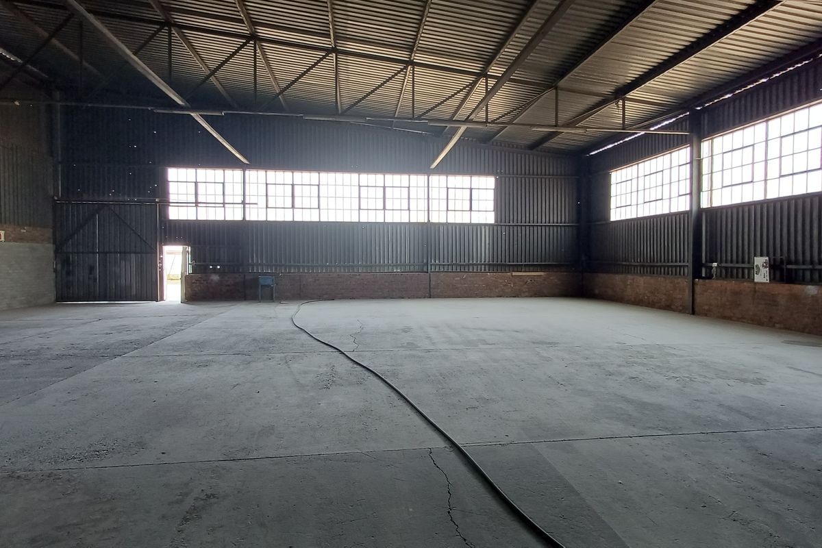 Spacious industrial warehouse unit featuring high ceilings with exposed steel trusses, concrete flooring, and large windows providing ample natural light.