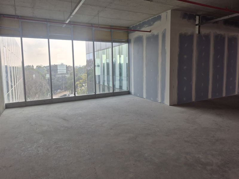 An unfinished open-plan office space featuring floor-to-ceiling windows, exposed concrete ceilings, and unpainted drywall partitions, ready for custom fit-out.