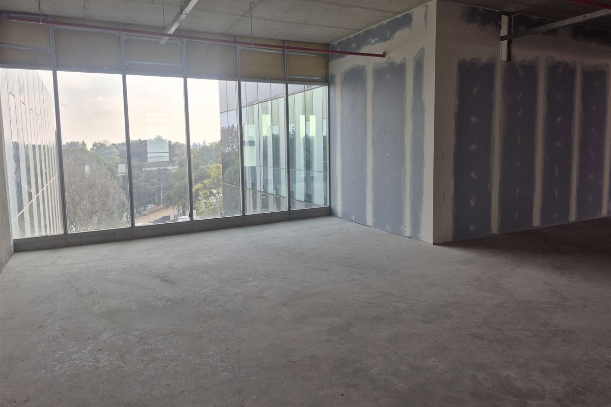 An unfinished open-plan office space featuring floor-to-ceiling windows, exposed concrete ceilings, and unpainted drywall partitions, ready for custom fit-out.