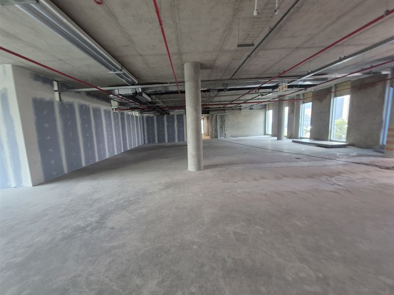 An expansive, open-plan office space in shell condition, featuring exposed concrete ceilings, support columns, and unfinished drywall partitions ready for custom fit-out.