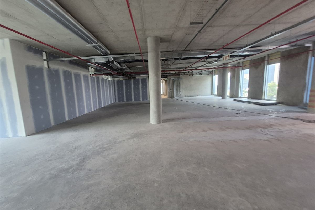 An expansive, open-plan office space in shell condition, featuring exposed concrete ceilings, support columns, and unfinished drywall partitions ready for custom fit-out.