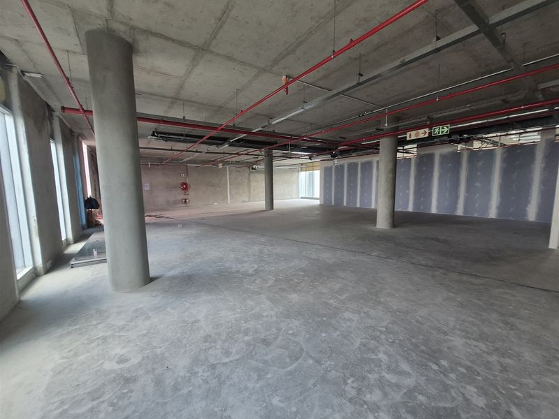 An expansive, open-plan office space in shell condition, featuring exposed concrete ceilings, structural columns, and large windows providing ample natural light.