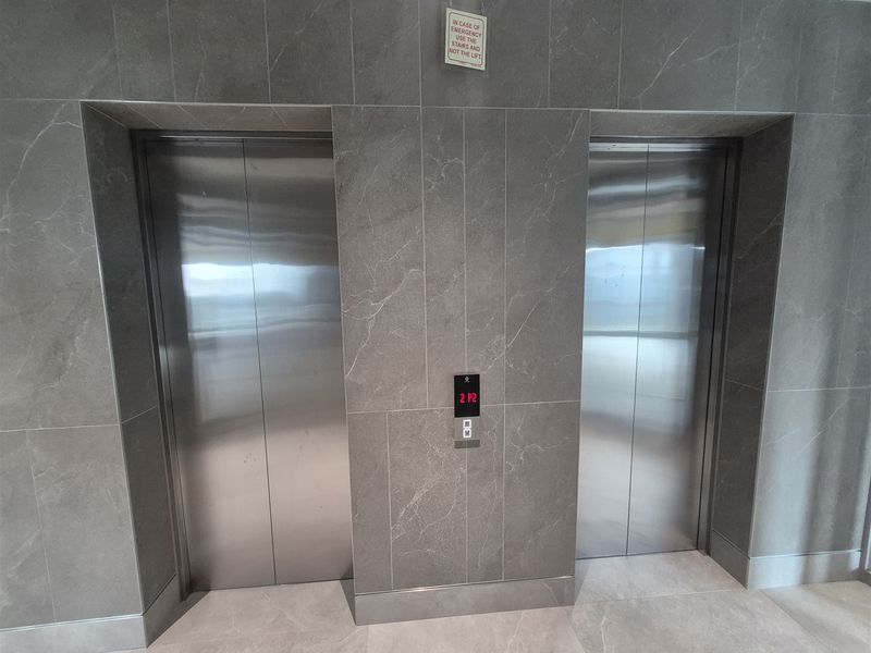 Modern office building elevator lobby featuring sleek stainless steel lift doors and high-quality grey marble-effect porcelain wall tiling.