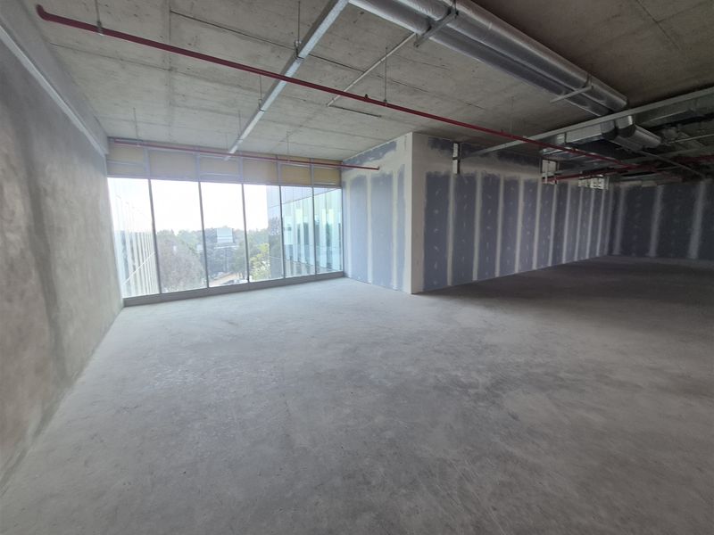 An expansive, open-plan office space in shell condition, featuring exposed concrete ceilings, large windows, and unfinished drywall partitions ready for custom fit-out.