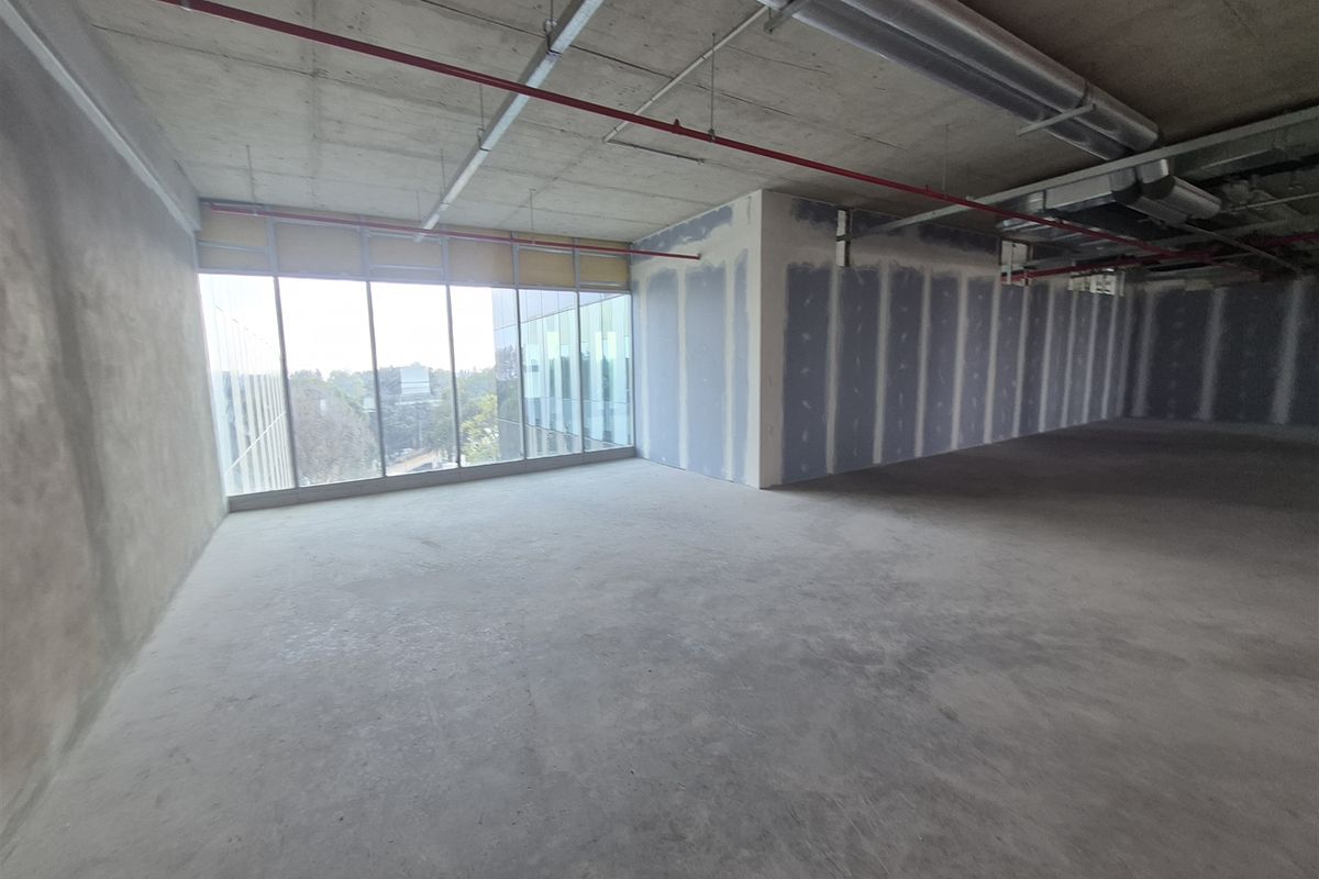 An expansive, open-plan office space in shell condition, featuring exposed concrete ceilings, large windows, and unfinished drywall partitions ready for custom fit-out.