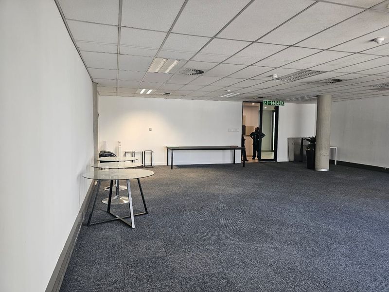 A spacious, open-plan office area featuring a suspended ceiling, recessed lighting, and carpeted flooring, providing a versatile workspace environment.