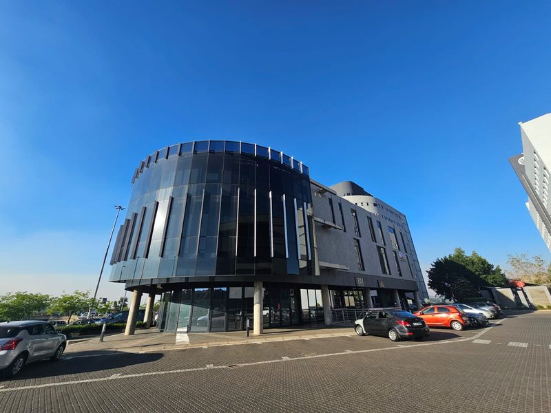 Modern multi-story office building featuring a prominent curved glass facade and integrated ground-level parking area.