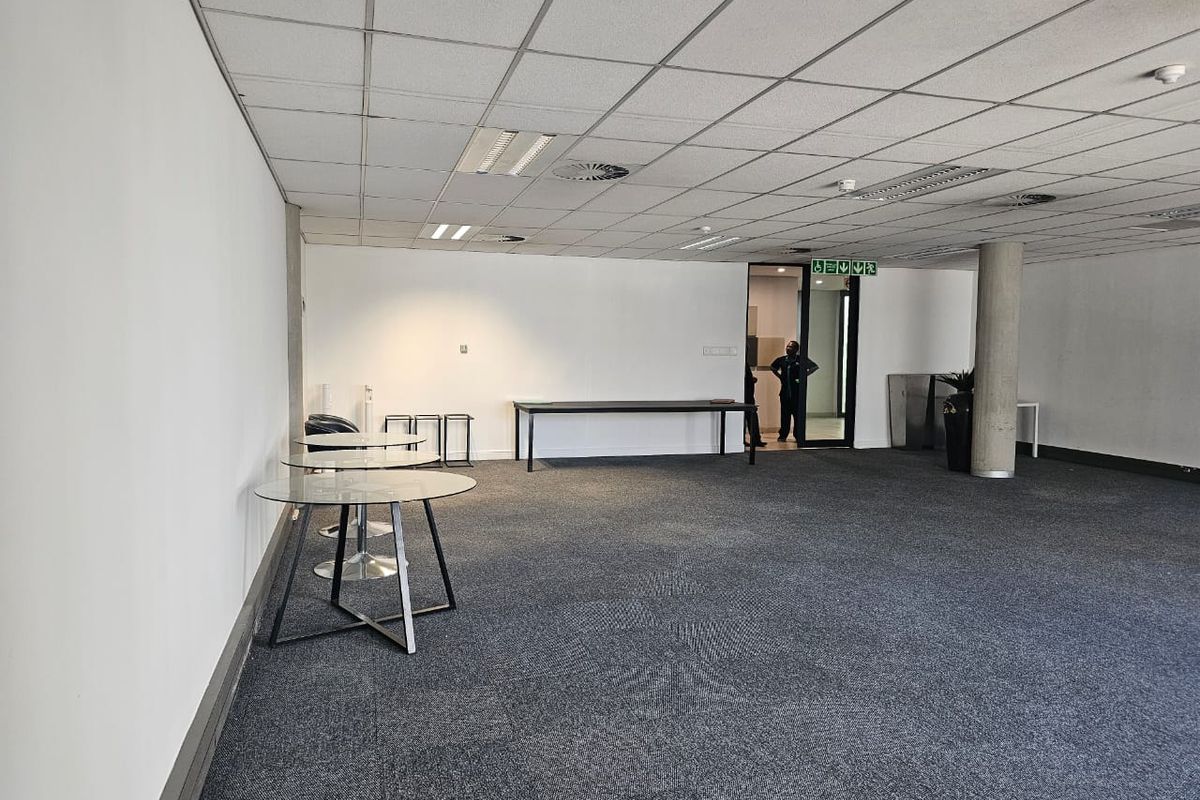 A spacious, open-plan office area featuring a suspended ceiling, recessed lighting, and carpeted flooring, providing a versatile workspace environment.