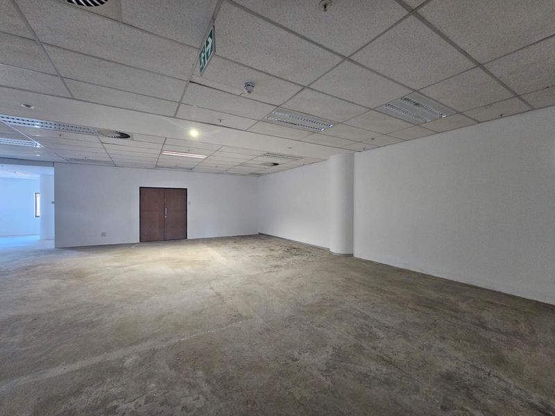 A spacious, empty office area featuring a suspended ceiling with recessed lighting and exposed concrete flooring, ready for custom fit-out.