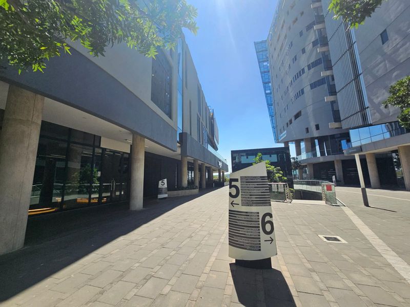 Modern office complex exterior featuring paved walkways, glass facades, and clear directional signage between buildings.