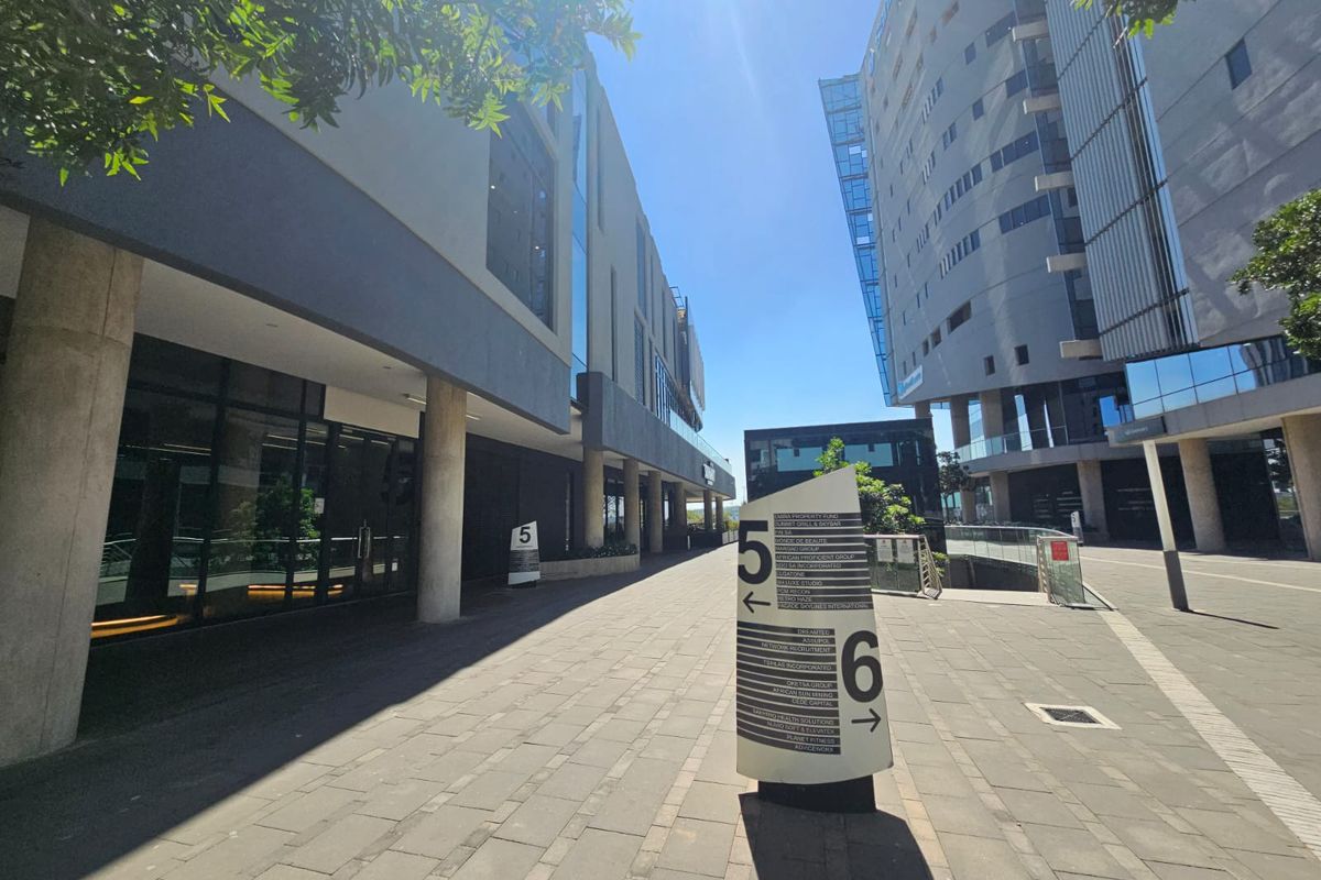 Modern office complex exterior featuring paved walkways, glass facades, and clear directional signage between buildings.