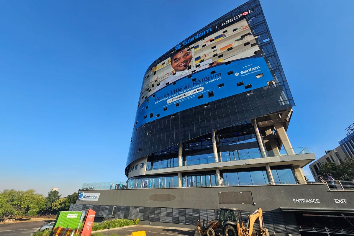 Modern multi-story commercial office building featuring a glass facade, prominent advertising signage, and ground-level parking access.