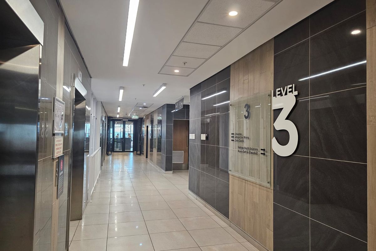 A modern, well-maintained office building hallway featuring tiled flooring, stainless steel elevator access, and clear directional signage for level three.