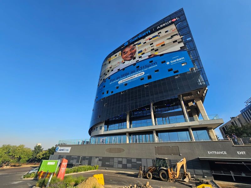 Modern multi-story commercial office building featuring a glass facade, prominent advertising signage, and ground-level parking access.