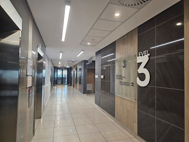 A modern, well-maintained office building hallway featuring tiled flooring, stainless steel elevator access, and clear directional signage for level three.
