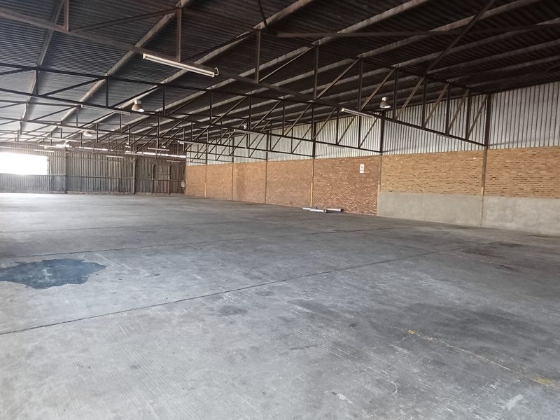 Spacious industrial warehouse unit featuring high exposed steel roof trusses, durable concrete flooring, and brick masonry walls, suitable for storage or manufacturing operations.
