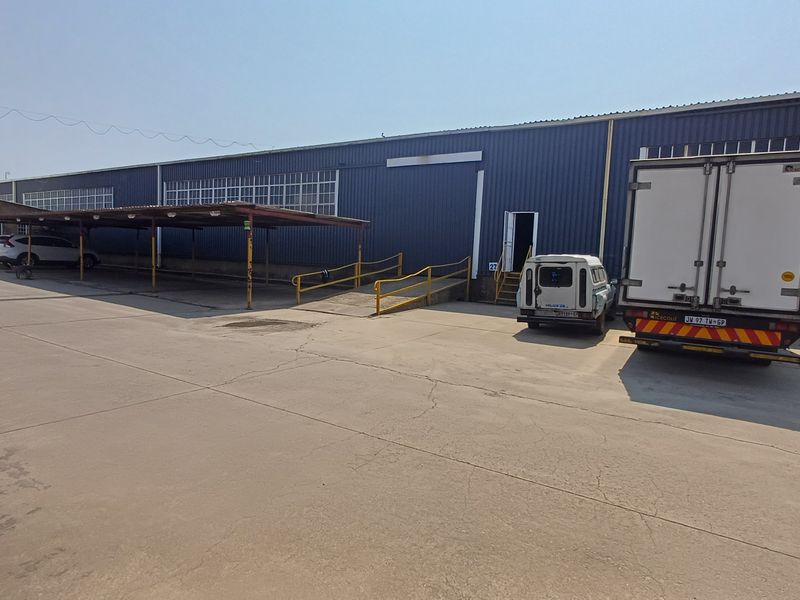 Industrial warehouse exterior featuring corrugated metal cladding, a concrete yard, a covered carport area, and a metal access ramp for loading.