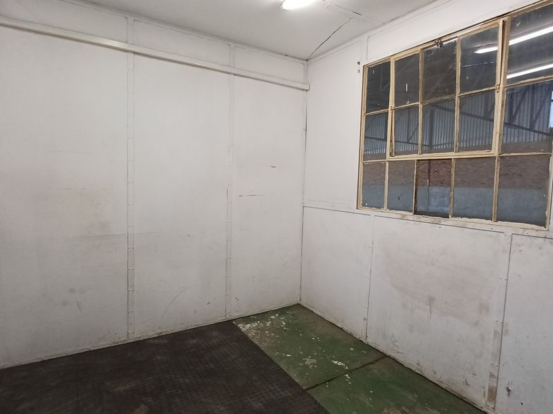 A functional utility space featuring industrial wall paneling, a metal-framed window, and exposed electrical conduit, suitable for storage or workshop use.