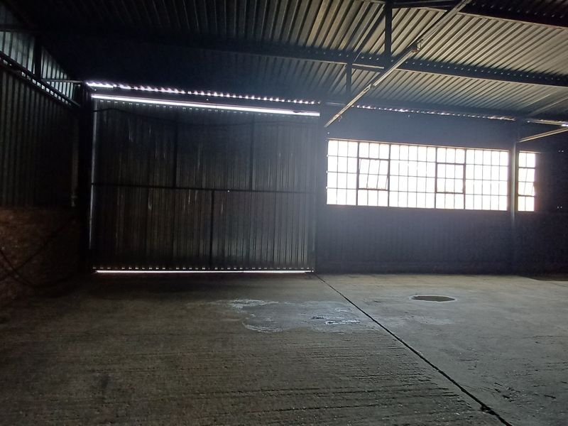 Spacious industrial utility area featuring concrete flooring, exposed steel roof structure, and large metal sliding doors with natural light from industrial windows.