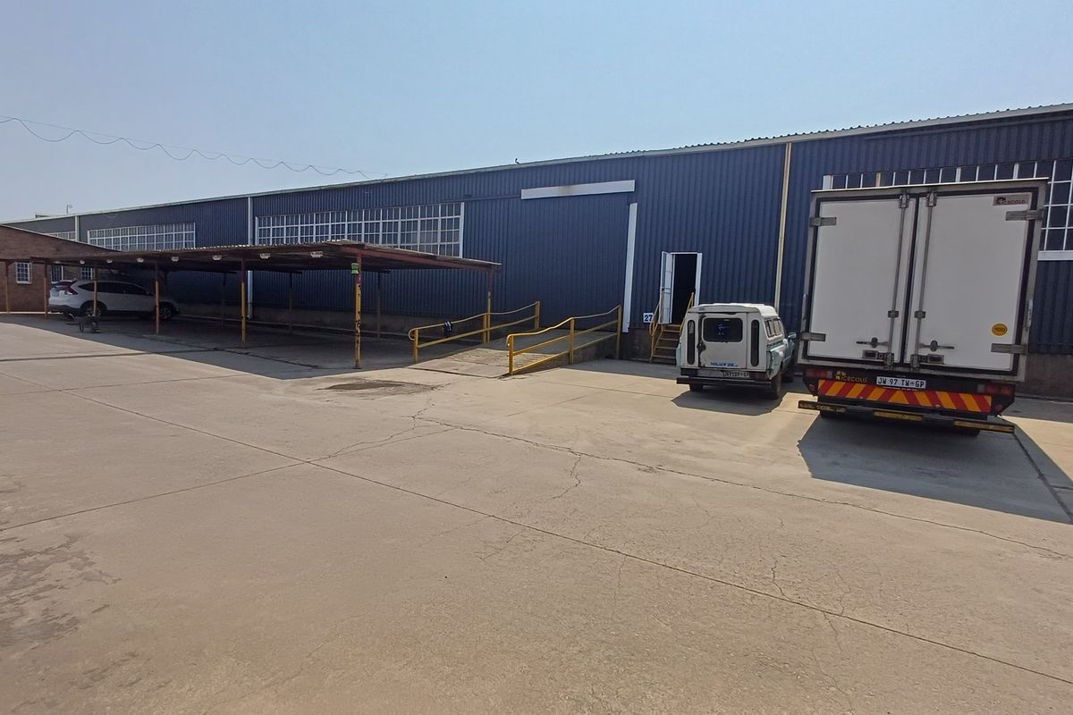 Industrial warehouse exterior featuring corrugated metal cladding, a concrete yard, a covered carport area, and a metal access ramp for loading.