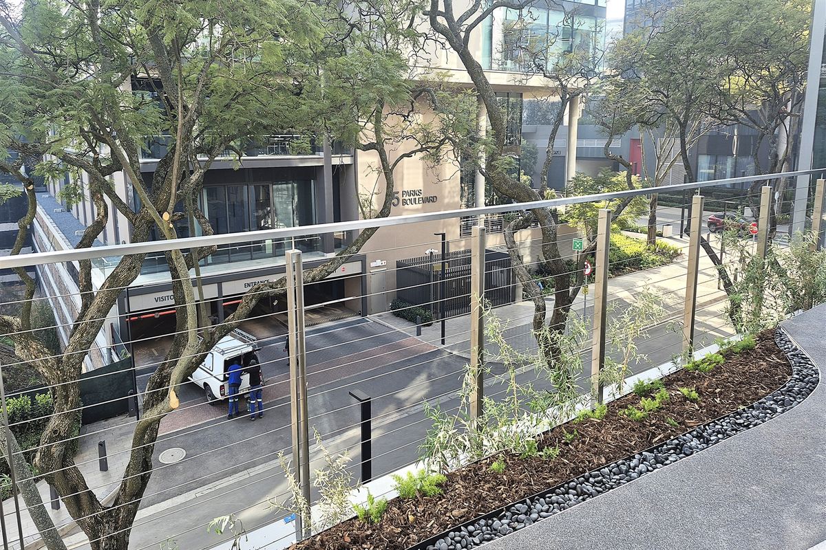 Elevated view overlooking the street entrance and surrounding office complex, featuring a modern stainless steel and wire cable balustrade with landscaped garden borders.