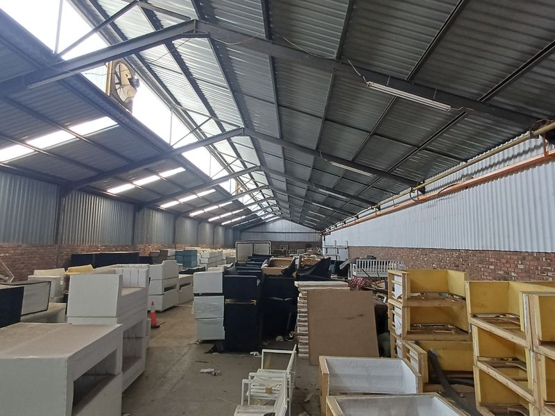 Spacious industrial warehouse featuring high ceilings with exposed steel trusses, skylights for natural light, and durable brick and corrugated metal wall construction.