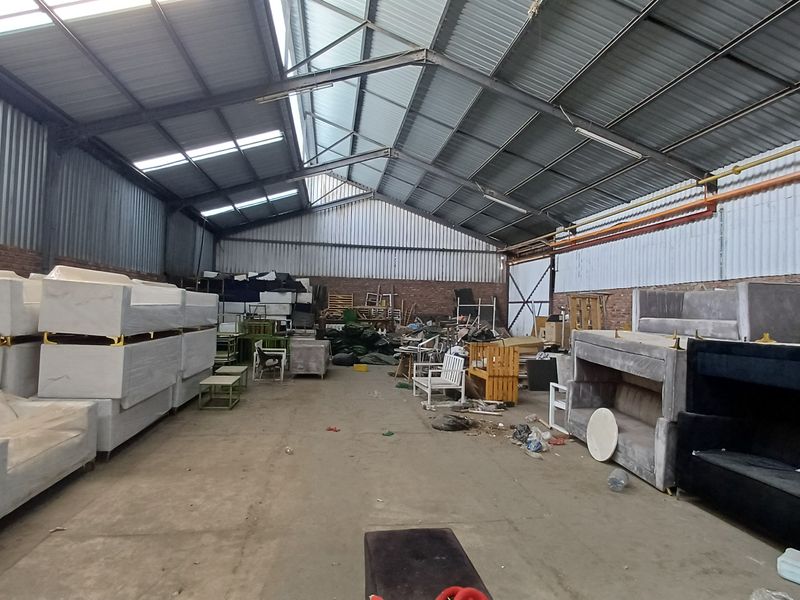 Spacious industrial warehouse unit featuring exposed steel trusses, corrugated metal roofing, brick walls, and durable concrete flooring, suitable for storage or manufacturing operations.