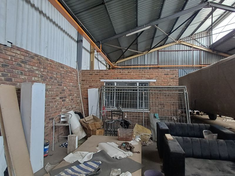 Industrial utility space featuring exposed brick walls, high-clearance corrugated metal roofing, and steel structural trusses, suitable for storage or workshop use.